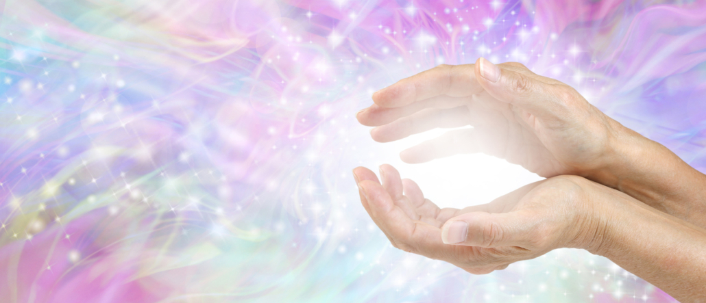 Photo of a female's cupped hands with white healing energy against a colourful blue purple green sparkling chaotic background